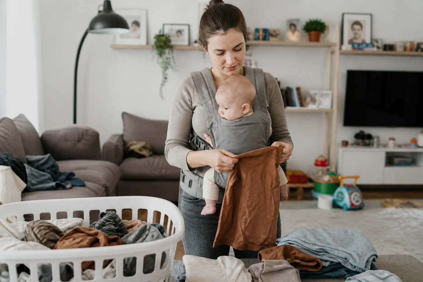 A parent wearing an infant in a supportive carrier while folding laundry at home
